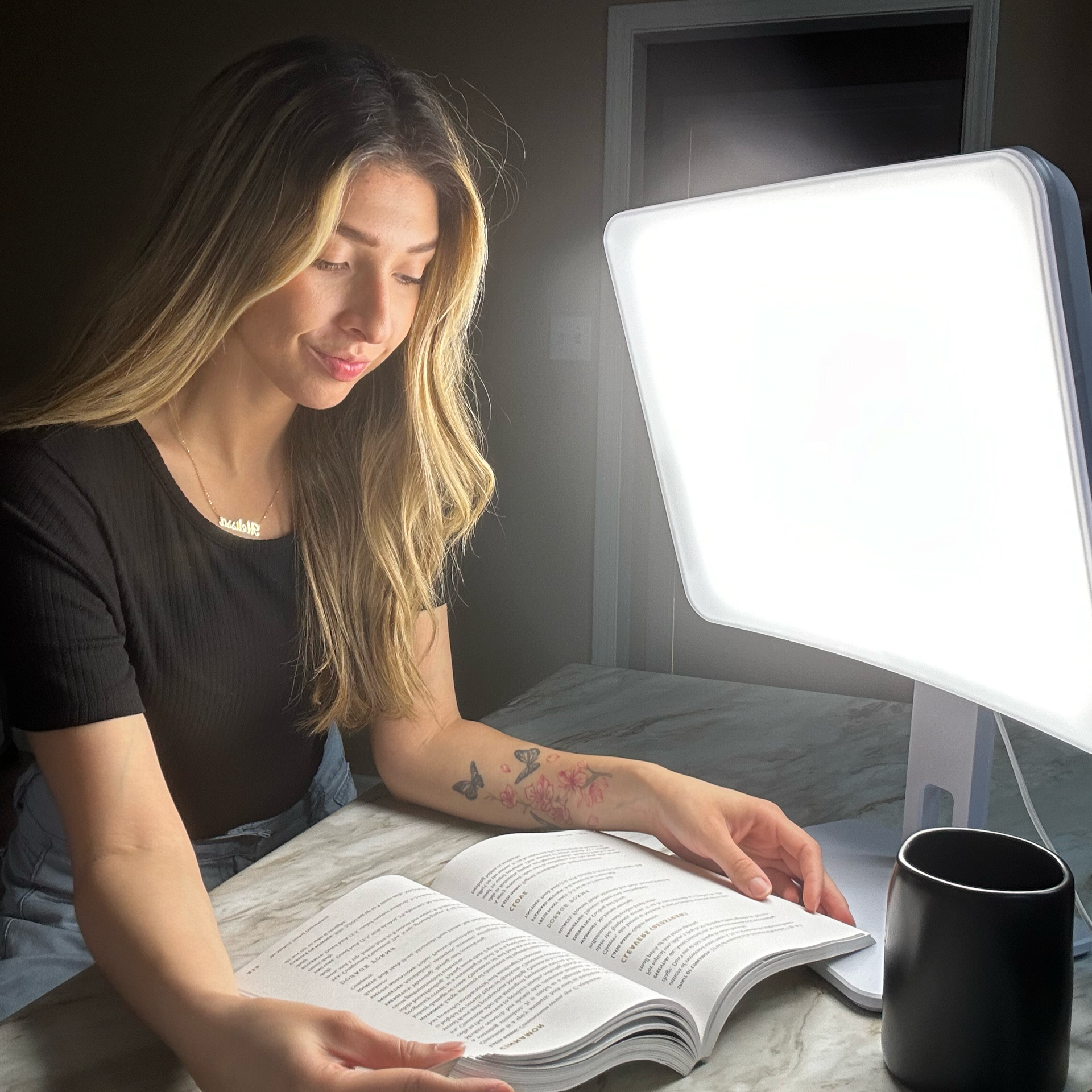 A woman reading next to a white light therapy lamp