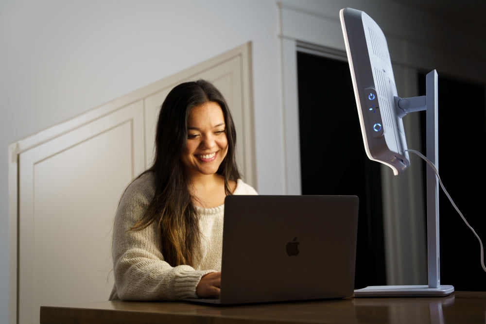 A woman sitting in front of a laptop using a SAD lamp