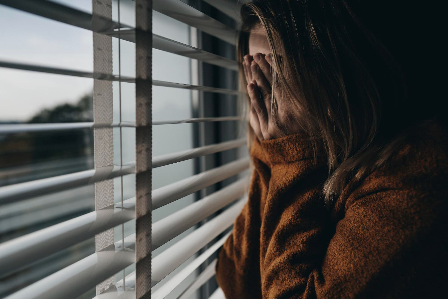 A woman with her hands on her face next to a window
