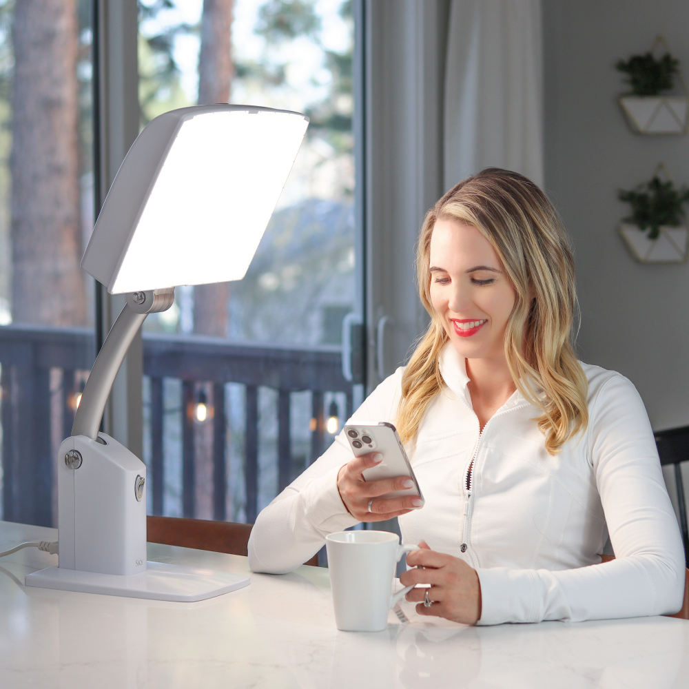 A woman on her phone in front of a white therapy lamp