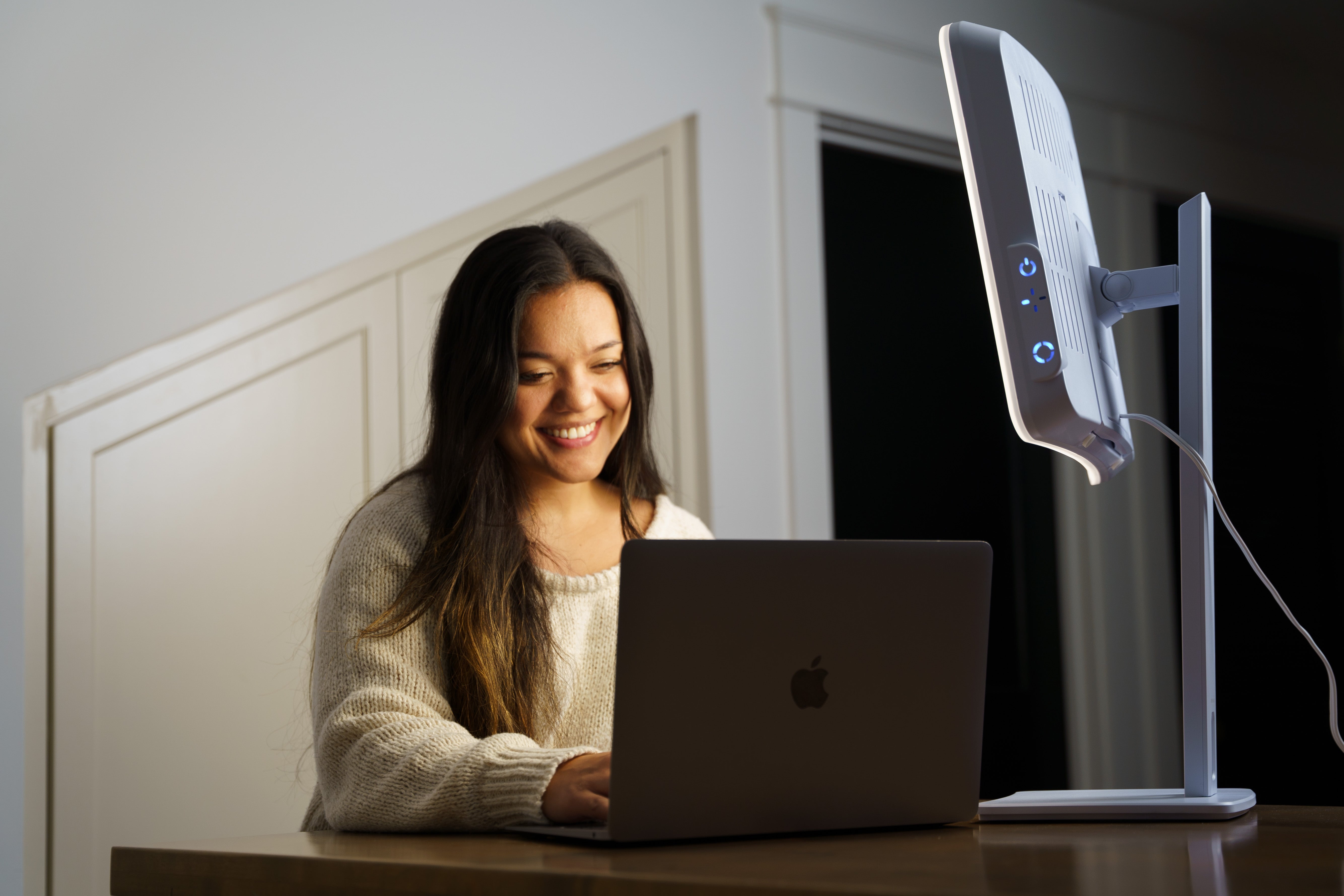 A smiling woman on her laptop in front of a therapy lamp